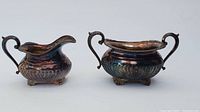Both creamer and sugar bowl showing overall shape, handle design, and tarnished silver surface