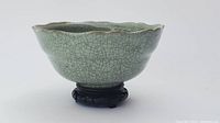 Side angle view of celadon crackle glaze bowl on carved wooden stand