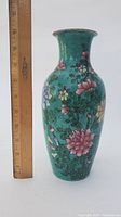 Full view of the vase next to a ruler showing it is about 10 inches tall with floral decoration.
