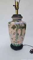 Front view of the Chinese porcelain lamp showing hand-painted crane and nature motifs with brass fitting and black wooden base.