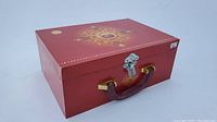Red decorative metal box with brown handle, latch, and gold accents storing the tea set