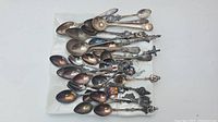 Top view of the full group of about 20 collectible spoons spread out on a clear surface, showing various decorative handles and designs.