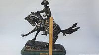 Full view of bronze cowboy and horse sculpture with wooden ruler for scale