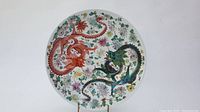 Top-down photo of the large round ceramic platter showing red and green dragons with floral patterns on white background.