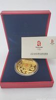 Gold plated medal displayed in open red box with navy interior and accompanying certificate card.