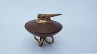 Front side view showing the wooden disc-shaped body and brass lighter top with three brass looped feet base.