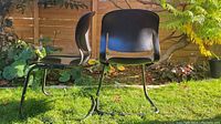 Side and back view of two vintage black fiberglass Herman Miller chairs with sled style metal base outdoors on grass showing shape and structure