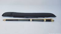Full view of the disassembled pool cue and black soft carrying case side-by-side.