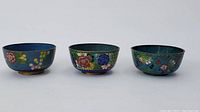 Three Chinese cloisonne bowls from side view showing floral patterns on blue and green backgrounds.