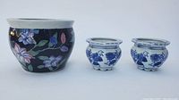 Three Chinese porcelain flower pots, two small blue and white with floral motifs and one larger black with multi-colored floral design, shown side by side.