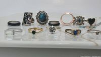 Twelve assorted rings shown on white surface, showcasing variety of designs and stones