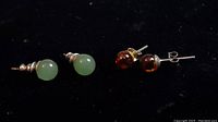 Two pairs of stud earrings: green jade studs on left and amber studs on right, both with metal posts