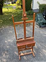 Full view of wooden artist's easel standing outdoors showing adjustable height frame and lower storage drawers.