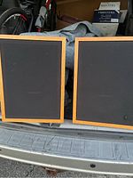 Front view of two speakers with black fabric grills and wooden frames.