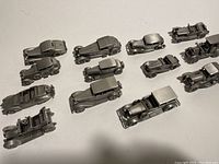 Overview of 13 pewter antique car miniatures arranged on white surface, showing varying models and styles with matte silver finish.