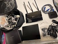 Full lot overview showing routers, Apple TV, cables, power supplies, and accessories including a pistol-shaped keychain.