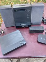 Lot layout image showing Sony CD mini system with two speakers, Sony Blu-ray player, Apple TV, and Bluetooth speaker placed on a table outdoors.