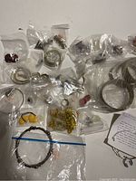 Overview of the lot showing multiple small plastic bags containing various rings, bracelets, earrings, and a watch.