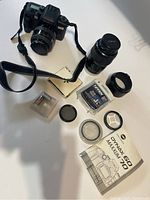 Minolta Maxxum 70 camera body with 35-70mm lens attached, accessories like filters, prism, battery, and manuals laid out on white surface.
