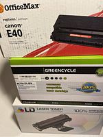 Photo showing three different laser toner cartridge boxes stacked, including OfficeMax Canon E40, Greencycle MLT-D115L-2PK, and LD Laser Toner.