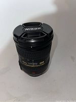 Front view of Nikon 18-200mm lens with cap on, showing Nikon brand and focal length markings.