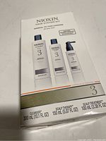 Front view of Nioxin Hair System Kit 3 box showing the three included products: cleanser, scalp therapy conditioner, and scalp treatment, with volume sizes and usage notes.