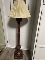 Full view of tall ornate floor lamp with carved wood or resin base and column, plugged in with cord visible on floor.