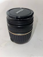 Front view of Tamron lens with Nikon lens cap on, showing black lens body with gold band and macro label.