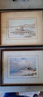 Photo of two framed antique paintings under glass, showing island and coastal castle scenes.