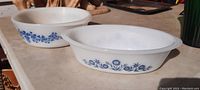 Two white glass baking dishes showing different blue floral patterns on a beige surface.