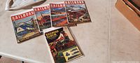 Four vintage railroad magazines laid out on a table, showing colorful illustrated covers with trains.