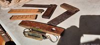 Photo of antique wooden folding rulers, carpenter's squares, wooden level with brass side, and small brass hanging scale arranged on a white surface.