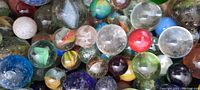 Close-up image showing a variety of antique glass marbles with different sizes, colors, and swirl patterns including clear, blue, green, red, yellow, white, and other shades.