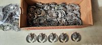Box filled with many vintage silvertone metal owl charms, plus several charms lined up in front, showing detailed owl design and size.