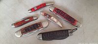 Top down view showing all six knives with varying handle colors and textures laid out on a flat surface.