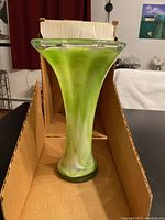 Front view of the vase showing flared, slightly scalloped top and swirled green and white coloring in the glass, standing inside a cardboard box.
