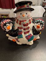 Front view of colorful holiday snowman cookie jar, holding two penguins.