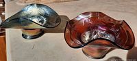 Two carnival glass bowls shown together on a flat surface, highlighting their distinct colors and fluted edges.