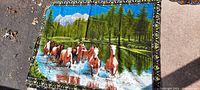 Tapestry showing group of horses running through water with pine forest and mountains background