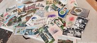 Spread of antique postcards on a table showing various scenes including holiday greetings, scenic views, floral designs, and real photo postcards.