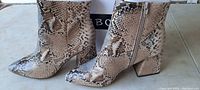 Left and right side view of Bamboo brand snake skin design women's boots showing block heels, pointed toes, and zipper sides.