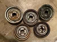 Five classic Austin Mini 10 inch tire rims viewed from one side, showing the bolt holes and various surfaces with rust and wear.