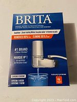 Front view of boxed Brita faucet water filtration system, showing brand, product type, chrome finish, filter lifespan of 4 months, and claims of removing 99% chlorine.