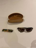 Maui Jim sunglasses laid out with hard case and folded cleaning cloth on white surface.