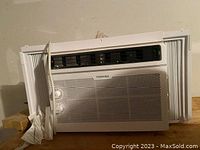 Front view of Toshiba window air conditioning unit showing control knobs, front perforated panel, and side accordion panels.