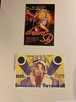 Photo of both movie posters, Liquid Sky with vibrant illustrated female figure and Battleship Potemkin with sailor and ship cannons in constructivist style on manila paper.