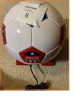 Top view of Coca-Cola mini fridge shaped like a soccer ball with power cord extended and auction tag attached