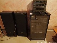 Full view of stereo system bundle showing the speakers, cabinet rack, and stack of stereo components.