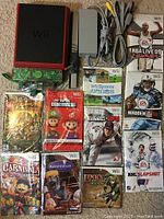 Photo of red Nintendo Wii console with power adapter, AV cables, 10 game cases arranged around it including Super Mario Bros. Wii, Pirates of the Caribbean, Wii Sports, MLB 2K9, and others.