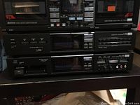 Three vintage Sansui stereo components stacked: double cassette deck on top, tuner in middle, and equalizer on the bottom, all on a dark surface.